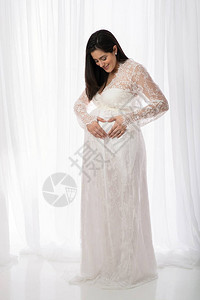 一个穿着白色蕾丝全长透明礼服的漂亮孕妇的画像她微笑着低头图片