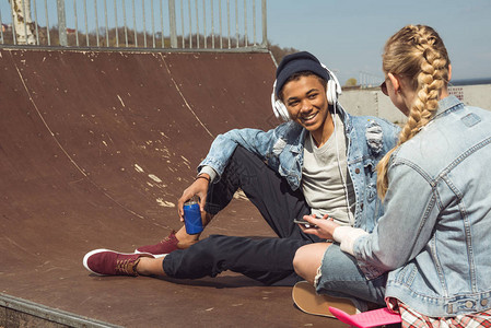 夫妇用耳机和在滑板公园抽打青少年有乐趣概念的听音乐图片