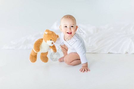 可爱的小男孩的肖像带着泰迪熊在床上玩耍图片