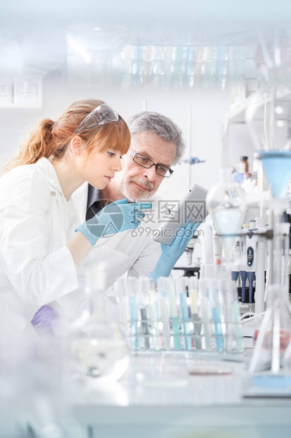 在生命科学实验室工作的医疗保健研究人员年轻女研究科学家和高级男主管专注于平板电脑屏幕评估和图片