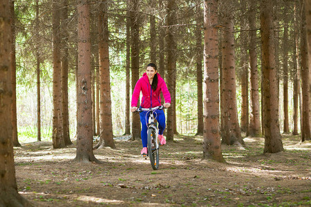 在一个年轻运动女子的夏日森林里骑着自行车穿过图片