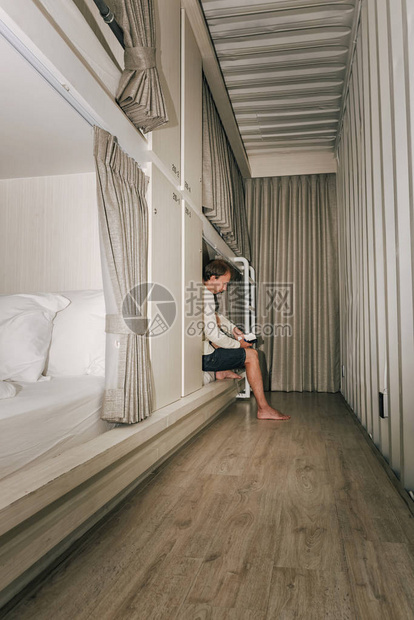年轻男子在旅馆房间阅读书有双层床晚上图片