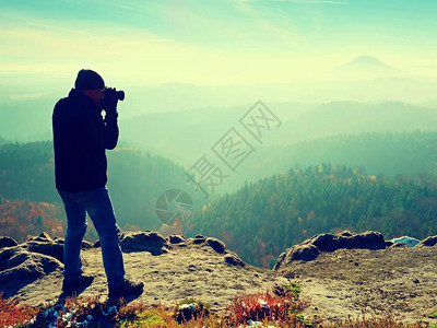 专业摄影师在岩石峰顶用镜子相机拍照图片
