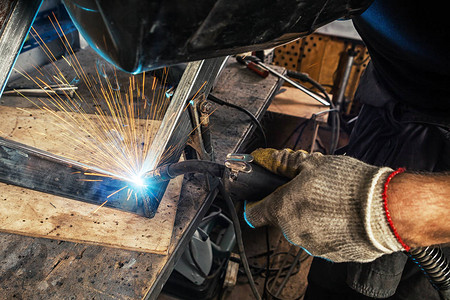 一名戴黑色焊接面罩和建筑手套的青年男子焊接工匠在一个车间焊图片