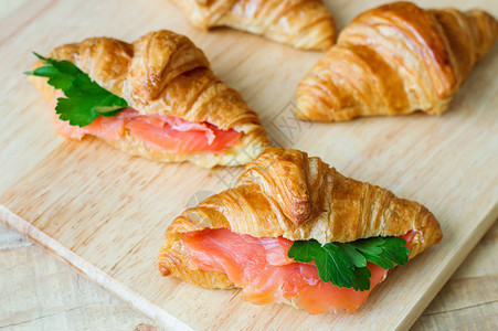 羊角面包三明治配鲑鱼和绿色欧芹木菜板上有红鱼的羊角面包健康的早餐开图片