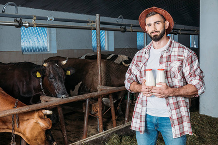 长着英俊胡子的农民拿着奶瓶装在摊间里背景图片