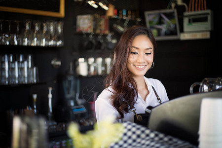 亚洲女咖啡师微笑着在咖啡店柜台使用咖啡机图片