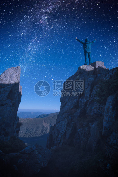 站在岩石悬崖边缘的人手举起来与夜景对峙在星般的天空中图片