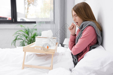 生病的妇女咳嗽和坐在床上用木托盘上配图片