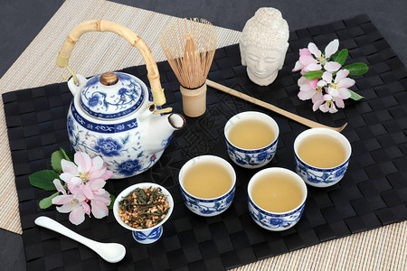 日本genmaichafujiyama茶道与东方茶壶干叶杯子拂子勺子佛头和春花在黑色垫子竹子图片