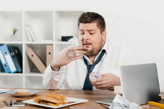 超重量体重商人在工作场所吃甜圈图片