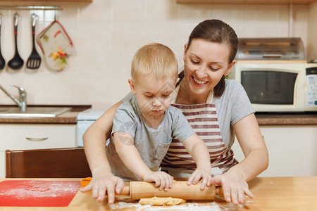 小男孩帮助妈在轻便的厨房里做圣诞姜饼3035岁的幸福家庭妈和23岁的孩子在家里擀面团并切饼干背景图片