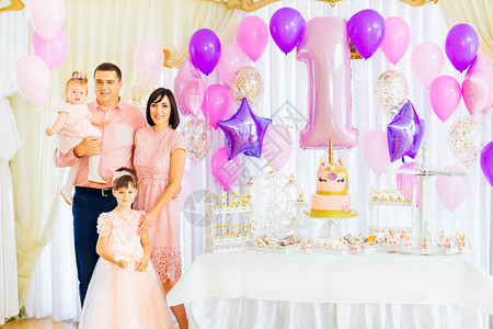 该家庭在一个带有蛋糕和充气球的节日装饰房庆祝孩子生日图片