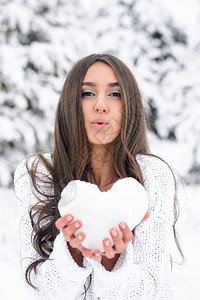 一位身穿白色蓬松套头衫的年轻女子握着雪中的心图片