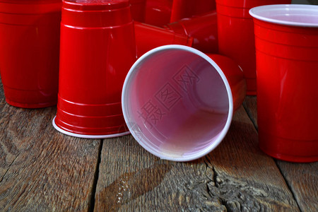 一张红色塑料杯的近距离图像在旧酒吧桌子上放着洒满啤图片