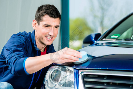 年轻人用吸水软毛巾干和擦亮清洁蓝色汽车表面图片