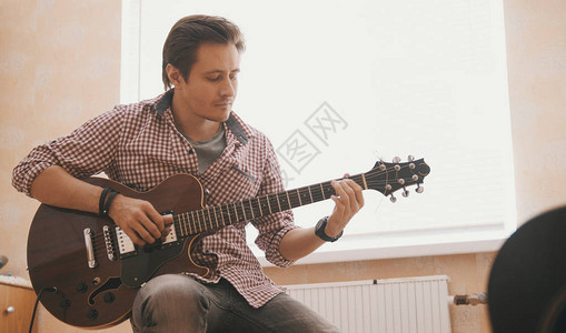 年轻小伙子音乐家在吉他上写音乐在厨房里演图片