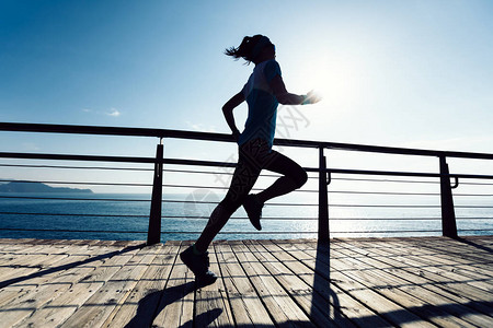 日出时在海边木板路上奔跑的健身女跑者图片