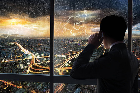商人在夜景城市景观和暴雨背景的大楼内玻璃窗上图片