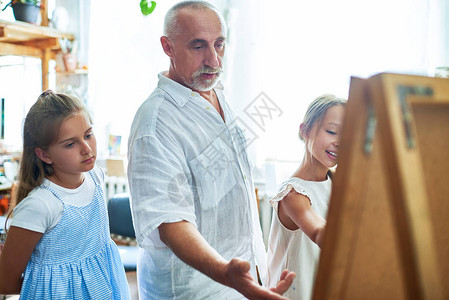 在艺术课上教授儿童绘画解释技巧和指向斜坡的成熟美术教师肖像背景图片