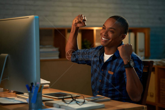 欢乐的非裔美国商人在坐电脑面前时举起手图片