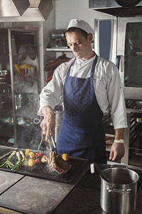 男厨师烹饪中型牛肉排和烧烤蔬菜图片