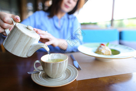 漂亮的女孩从茶壶里把茶倒进杯子里图片