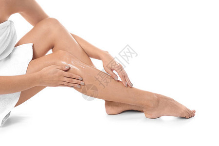 女人在白色背景下在腿上涂抹身体霜特写图片