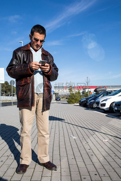 中年白人男子在停车场等待预约时查看智能手机图片