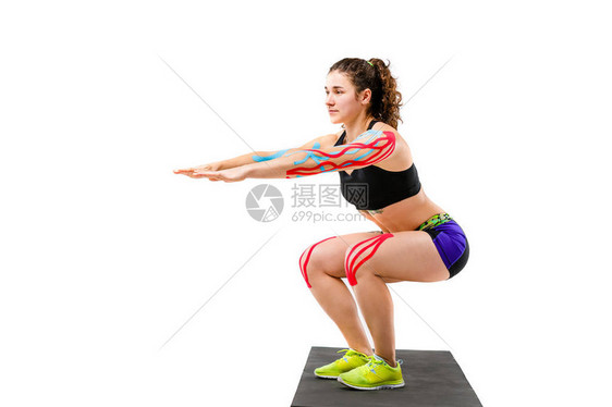 主题运动学磁带康复和运动员的健康美丽的女孩在孤立的白色背景上的黑色地毯上做深蹲运动在手臂和膝盖上图片