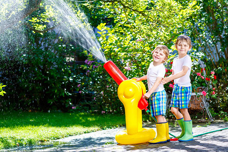 两个小男孩在炎热和阳光明媚的夏日玩花园软管洒水器图片