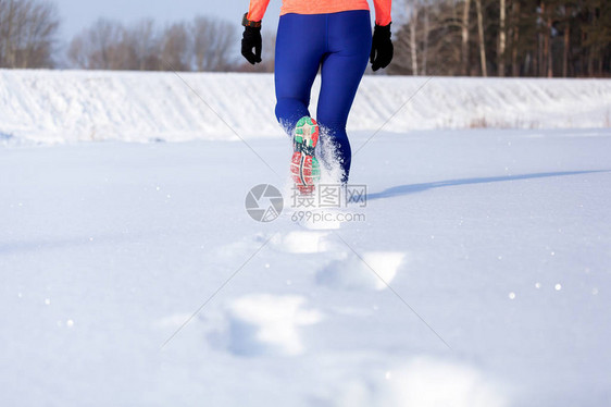 一个穿着亮紫色紧身裤和运动鞋的年轻女子在明亮的冬日穿过冬雪的特写镜头图片