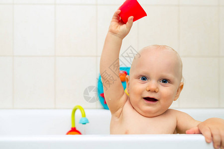 在浴缸里玩五颜六色的玩具微笑的小孩在浴室里看着相机婴儿玩耍图片