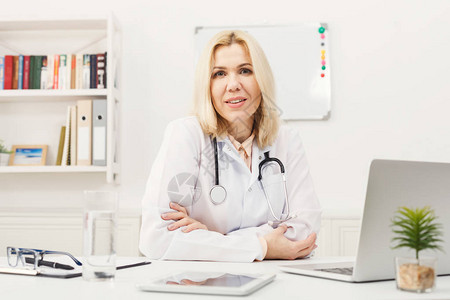 快乐的女医生用听诊器坐在桌面上的画像图片