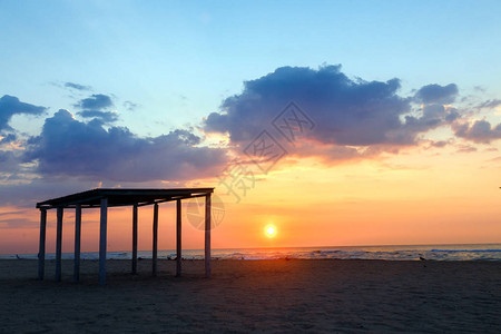 日落背景下空荡的沙滩上的剪影凉亭图片