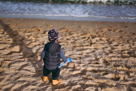 可爱的小男孩站在海边沙滩背景上拿着铲子图片