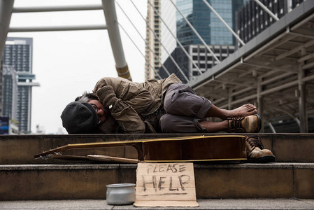 老乞丐或无家可归的脏人睡在现代城市的楼梯上图片