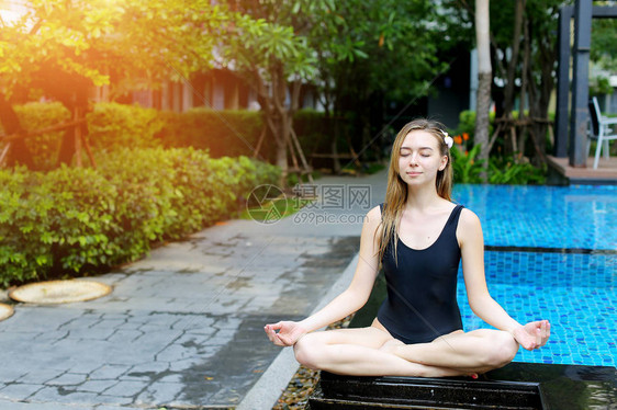 健身女人闭上眼睛坐在莲花位置在阳光明媚的日子在游泳池边做瑜伽身体或精神行为至高无上的存在或接图片