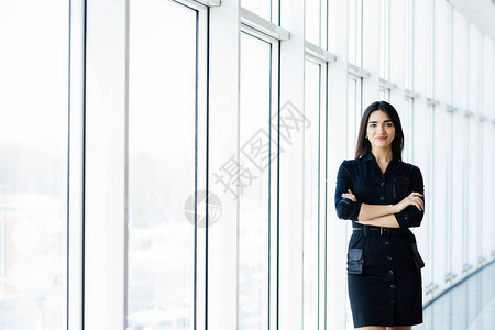 快乐的年轻女士的肖像与跨臂在商业中心窗口背景图片