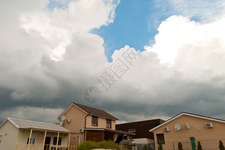 白色美丽蓬松的大云灰色暴雨风暴在蓝天的背景下在五颜六色的房子下面有不同的屋顶美丽的图片