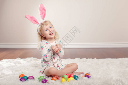 戴着复活节耳朵的可爱有趣的白人小女孩坐在工作室里柔软蓬松的地毯上带着节日彩蛋玩庆祝传统基督图片