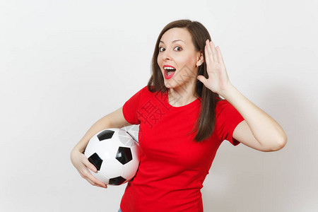 美丽的欧洲年轻女子足球迷或穿着红色制服窃听的球员听力手势拿着白色背景上孤立的足球体育踢足球健康健康的图片