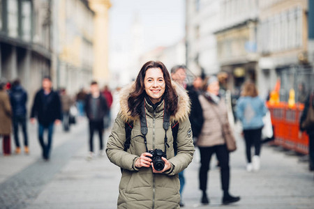 肖像美丽的年轻旅游女人在冬天站在德国慕尼黑一条中央街道上人群的背景中拿着一个黑色的大专图片