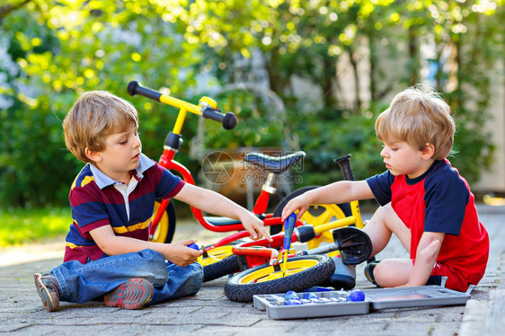 两个快乐的小男孩在自行车上修理链条并更换平衡自行车的轮子兄弟姐妹在户外使用工作具一起工作儿童双胞胎和兄图片