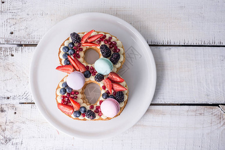 以白色奶油和草莓蓝和黑莓装饰的数字8形状的自制蛋糕甜品作为三月图片