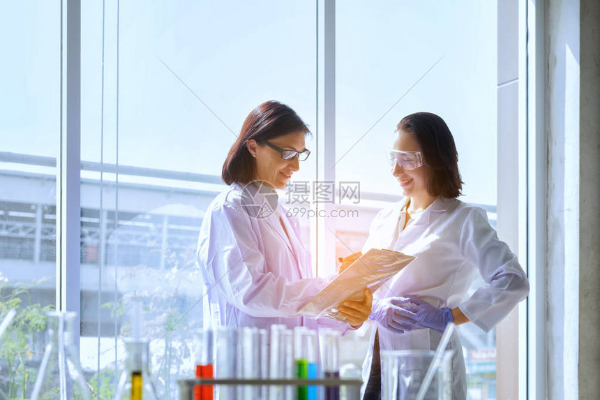 年轻的女科学家与技术人员站在实验室工作人员在现代实验室进行医学研究科学家持有带分析结果图片