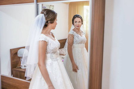 穿着婚纱的美丽的年轻新娘看着镜子图片