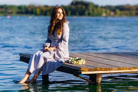可爱的姑娘坐在木头码上将脚浸在水图片