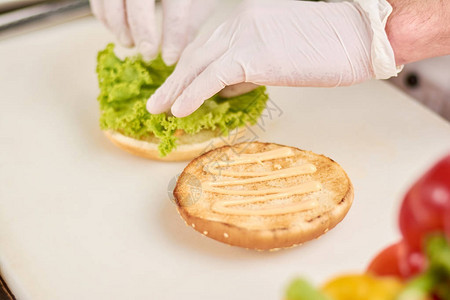 厨师在汉堡上加生菜叶厨师在专业厨房烹饪开胃汉堡烹图片