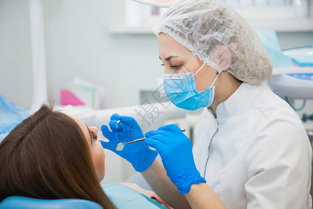 戴蓝色防护面罩的女口腔科医生检查病人的牙齿牙医在牙科诊所办公室进行龋齿治疗人医学口腔医背景图片